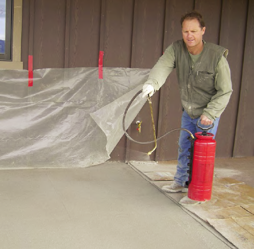 Doug Carlton sprays film onto a patio freshly colored with L.M. Scofield hardener. Next, he would stamp with an interlocking Arizona Flagstone pattern from Proline Concrete Tools. Gusts of up to 30 mph hit soon after this picture was taken, but the film held moisture fine and the imprint was consistent.