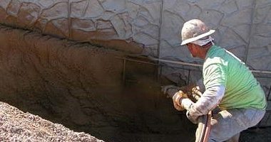 A concrete mason shoots shotcrete onto the wall with a pump.
