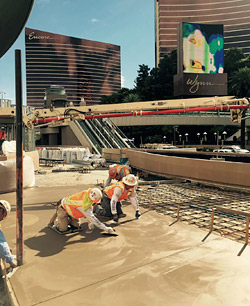 concrete construction workers hand troweling a large slab of setting concrete.
