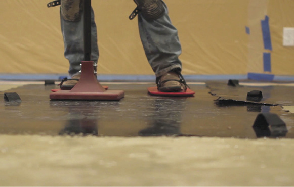 A tamper and texture skin shoes on a stamping mat at a concrete overlay training class.