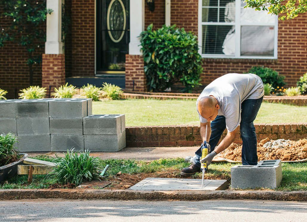Pour a level, 6-inch concrete slab using a 2-by-4 frame (or what the local building code requires) for a proper size footing. Secure each course of blocks with a high-strength anchoring epoxy, staggering the joints.