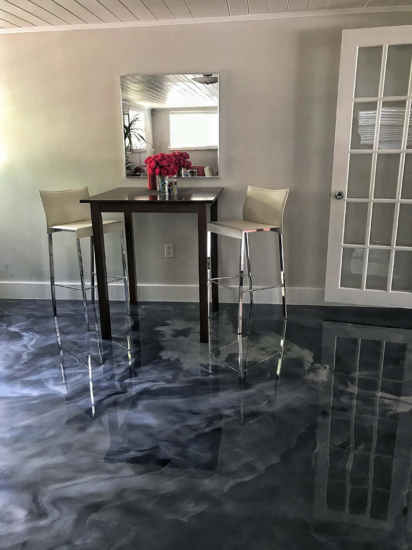 A tall table with tall chairs sit atop an epoxy floor. Colors dark blue and light gray create a swirl that looks like the ocean.