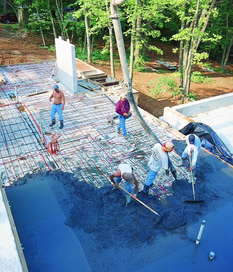 Team of concrete contractors spreading integral colored concrete over a floor with radiant heating tubes installed.