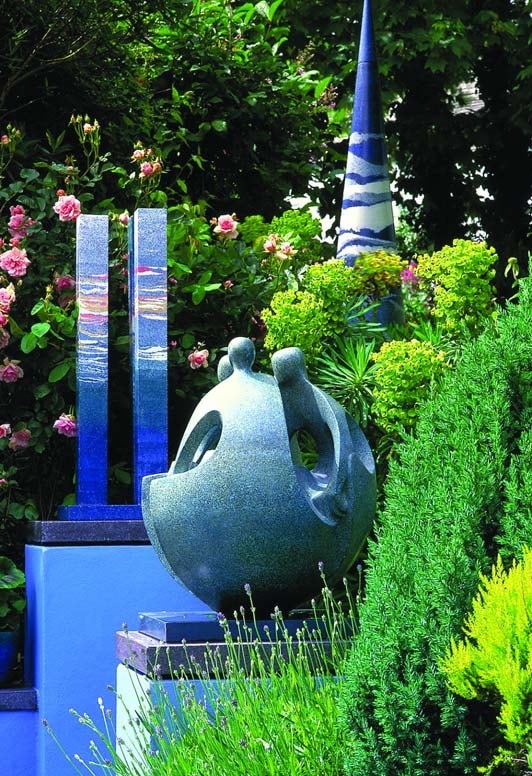 Concrete Sculpture in the center of a garden, round on the bottom with three people rising from the outside.