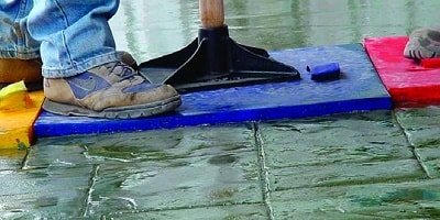 Dark green patterned concrete being stamped into a perfectly cured concrete slab.