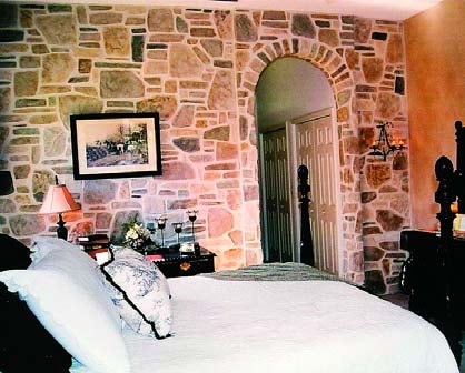 Bedroom with an arched entry into the bathroom sports an faux rock wall using a cementitious (concrete) vertical overlay that is stained and painted to look like rock and mortar.