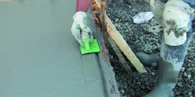 Construction worker using a handmade tool to finish the edge of a concrete slab.