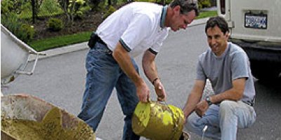 Two men mixing color from three buckets next to a dirty concrete covered wheel barrow.