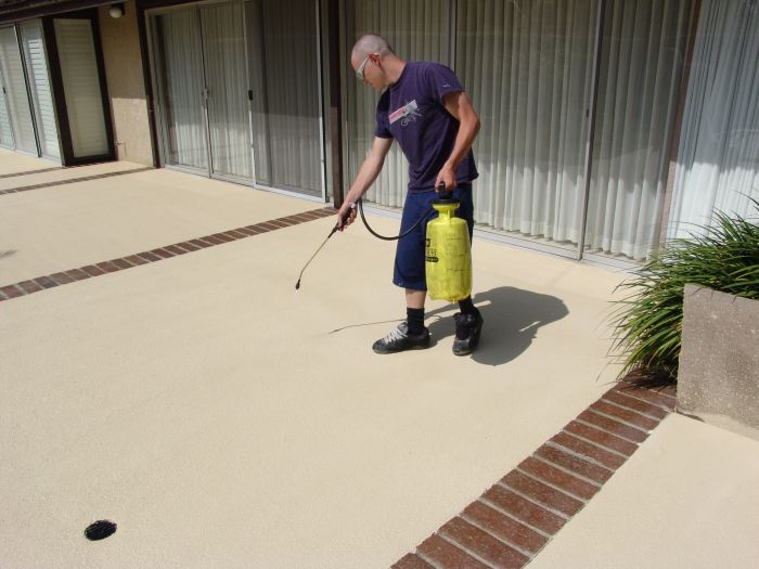 A person applying sealer to concrete with a sprayer