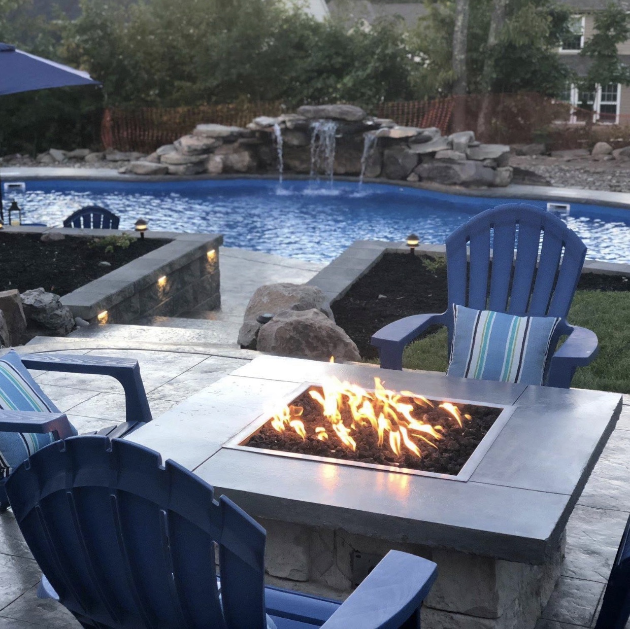 Outdoor patio space with a firepit in the forefront and the pool in the back.