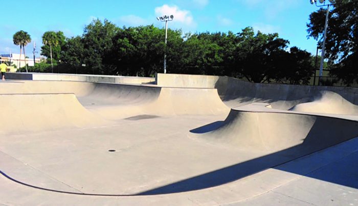 A skatepark with a backdrop of green trees and bright blue sky