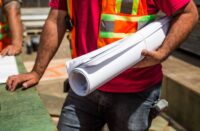 A person in a safety vest holding rolled up blueprints on the job site.