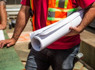 A person in a safety vest holding rolled up blueprints on the job site.