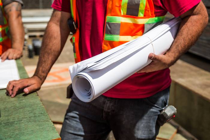 A person in a safety vest holding rolled up blueprints on the job site.