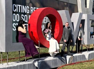A bride sitting in the O of a LOVE sculpture made of concrete