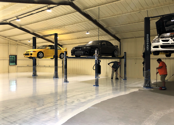 Applying Laticrete products on a concrete garage floor with cars elevated on car lifts above.