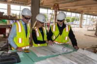 A group of students gathered around blueprints on a jobsite.