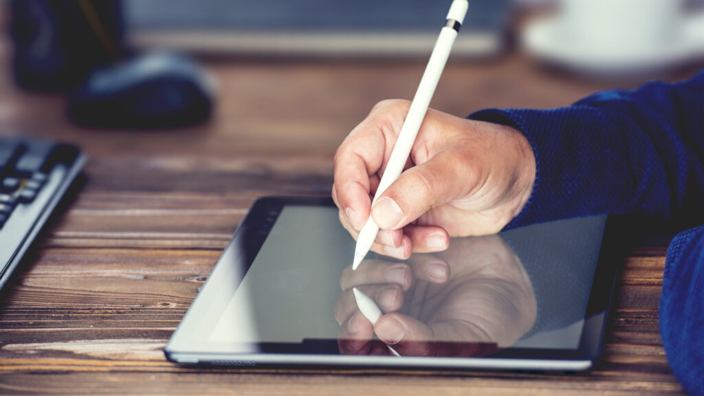 A person using a stylus to write on a tablet - using digital platforms is one way of adapting your business during COVID-19