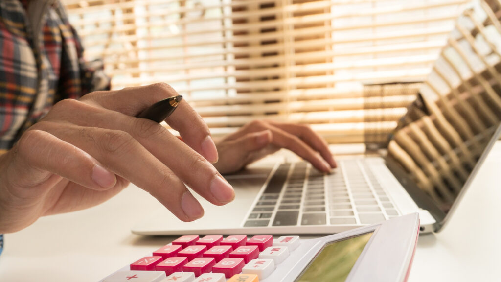 A person working at a laptop with a calculator nearby - using online resources is great for adapting your business during COVID-19