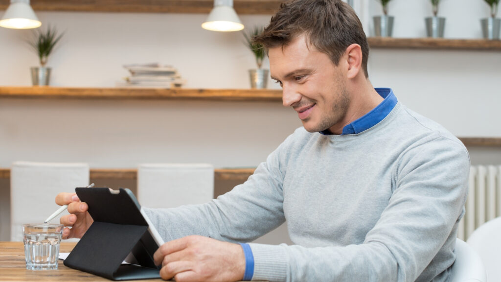 A man in a gray sweater sitting at a computer in his home.
