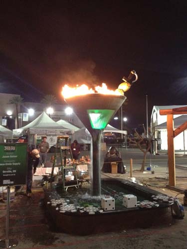 The martini glass made of concrete with water pouring down and flames coming from the top.