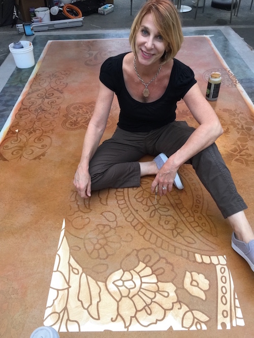 Melanie Royals with an in progress picture of a stencil being used on concrete.