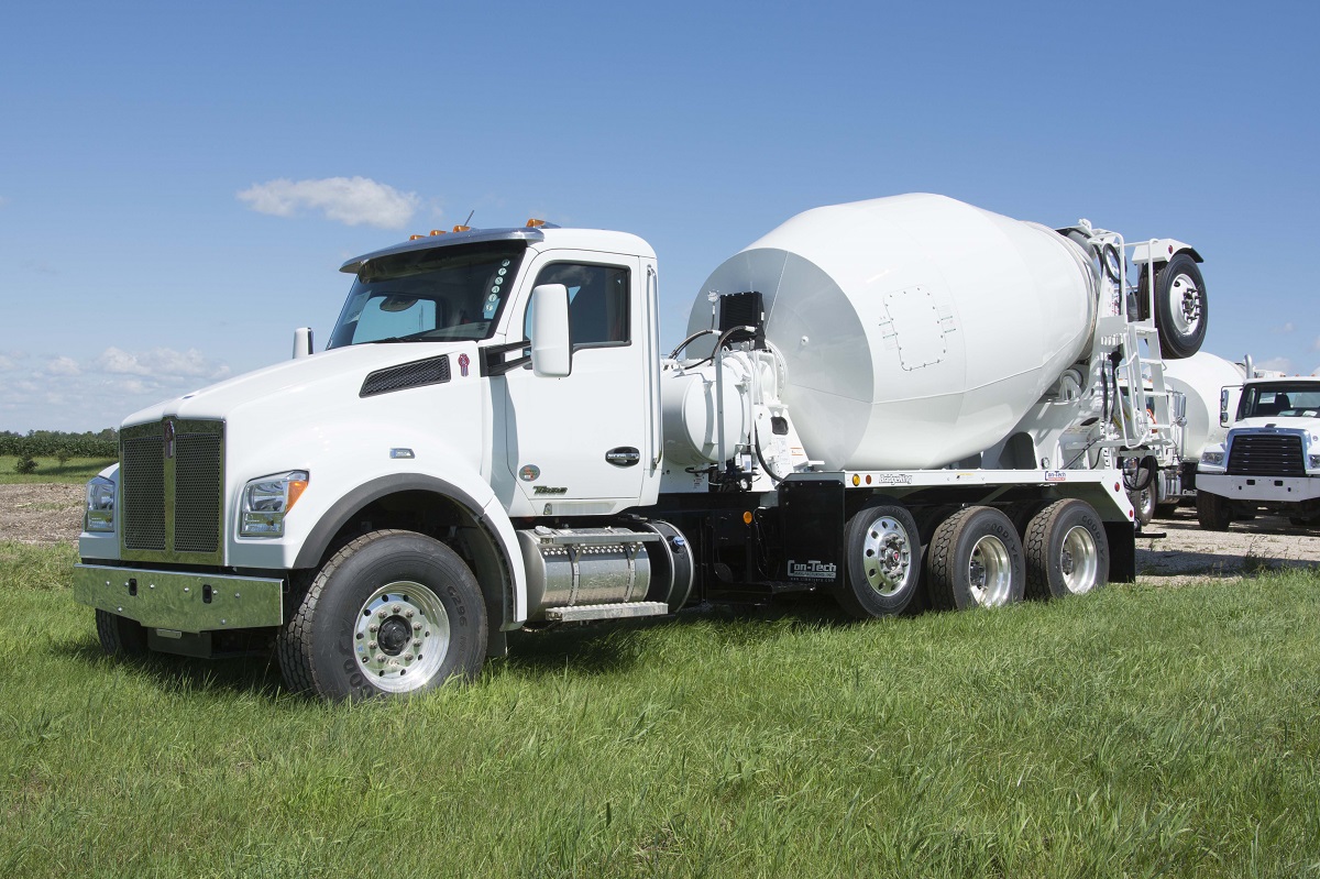 A concrete truck in a field of grass.