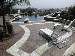 Texture-Crete cementitious overlay for all surfaces shown here on a pools deck using two colors has lounge chairs and a palm tree.